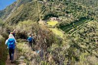 Hikers with backpacks hike down a narrow trail with Choquequirao terraces and stone buildings in view, Choquequirao Trek 5 Days 4 Nights | TreXperience