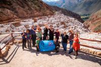 Group of travelers posing with a banner in front of white salt ponds of Maras | TreXperience