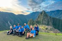 Group of travelers in blue shirts posing in front of Machu Picchu and the Andean mountains at sunset | TreXperience