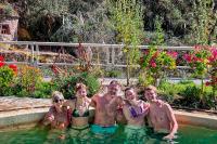 Group of travelers enjoying an outdoor hot spring pool surrounded by gardens and a mountain setting | TreXperience