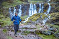 Hiker with trekking poles walking in front of a waterfall in a mountain landscape during a hike | TreXperience